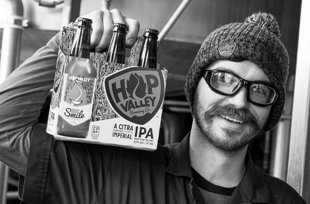 Hop Valley employee holding up a six pack of Big Smile IPA bottled beer